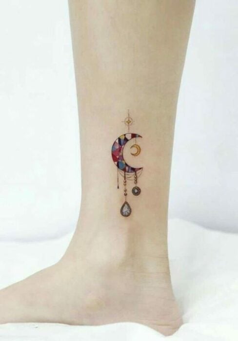 tatuaje de una luna con algunos diamantes colgados en el costado del pie de una persona 