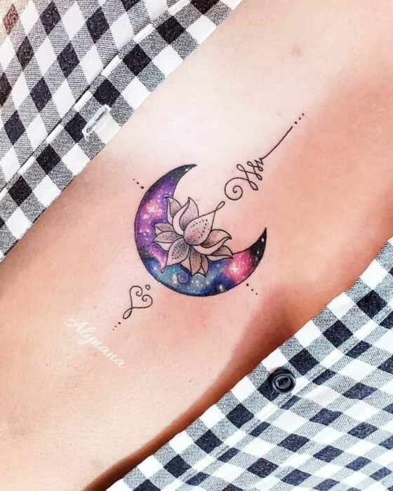 poitrine d'une personne avec un tatouage en forme de lune avec une fleur aux couleurs violet et rose 