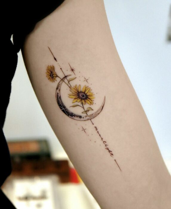 brazo de una chica mostrando el diseño de tatuaje de una luna con un par de girasoles 