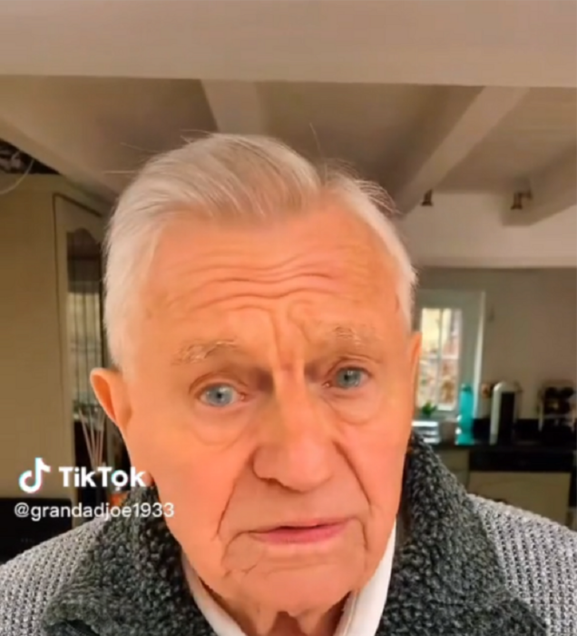 un abuelito caucásico mirando hacia la cámara está en su casa y lleva un suéter de color gris