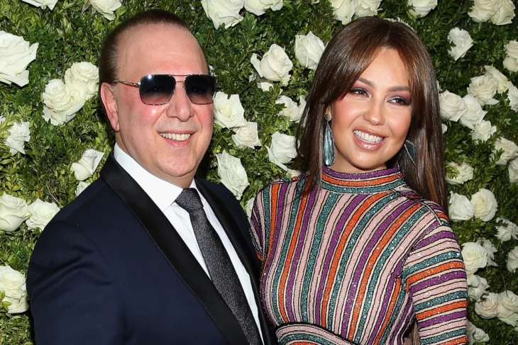 Thalía y Tommy Mottola fotografiados con un fondo lleno de rosas blancas ambos visten de gala