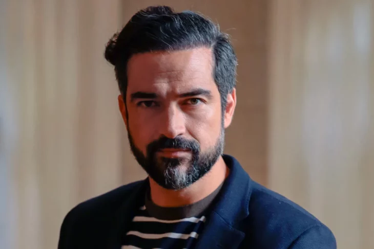 Alfonso Herrera in the foreground has a beard and mustache and looks directly into the camera