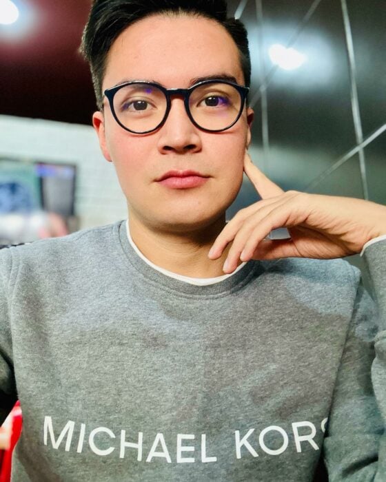 selfie photograph of a young man dressed in a gray shirt with glasses with his manol on his chin 
