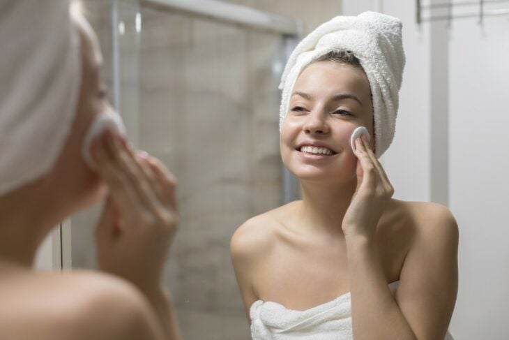 fotografía de una chica limpiando su rostro frente al espejo 