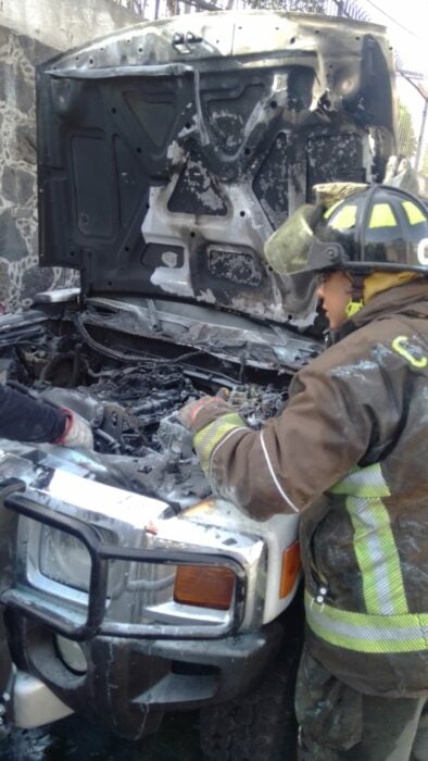 Firefighter looking inside the hood of a van on fire in the middle of the street 