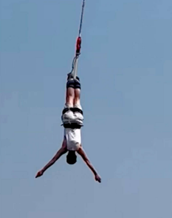 un hombre cayendo en un salto de bungee lleva los brazos extendidos y los pies amarrados por la cuerda de seguridad