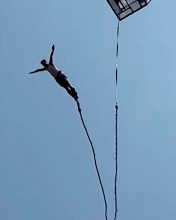 un hombre saltando del bungee lleva los brazos extendidos y los pies amarrados a la cuerda de seguridad