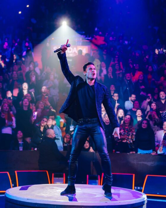 Carlos Rivera posando con la mano arriba en medio de un escenario frente al público en un concierto 