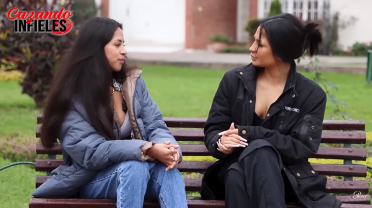 two women talk sitting on a garden bench both are wearing casual clothes