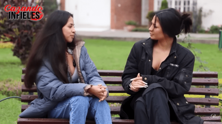 dos mujeres platican sentadas en la banca de un jardín ambas llevan ropa casual