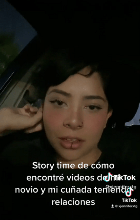 una chica mira a la cámara mientras habla tiene en el rostro una mueca de tristeza esta en su auto y lleva ropa oscura