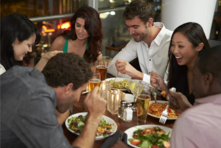 un grupo de amigos cenando en un restaurantes varios de ellos están tomando cerveza y en sus platos tienen diferente comida todos se ven muy contentos