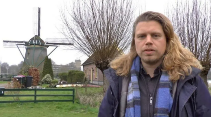 un hombre caucásico posa en una de las calles de Holanda lleva ropa de invierno y tiene el cabello largo