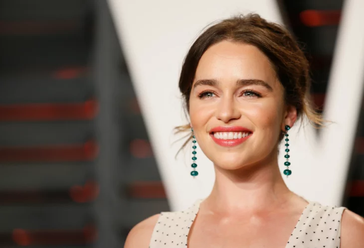 Emilia Clarke posa en una alfombra roja con un vestido de tono claro lleva el cabello recogido en un chongo