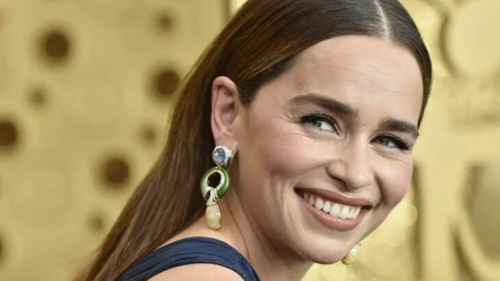 Emilia Clarke sonríe a la cámara posando de lado en un evento de Hollywood lleva largos aretes