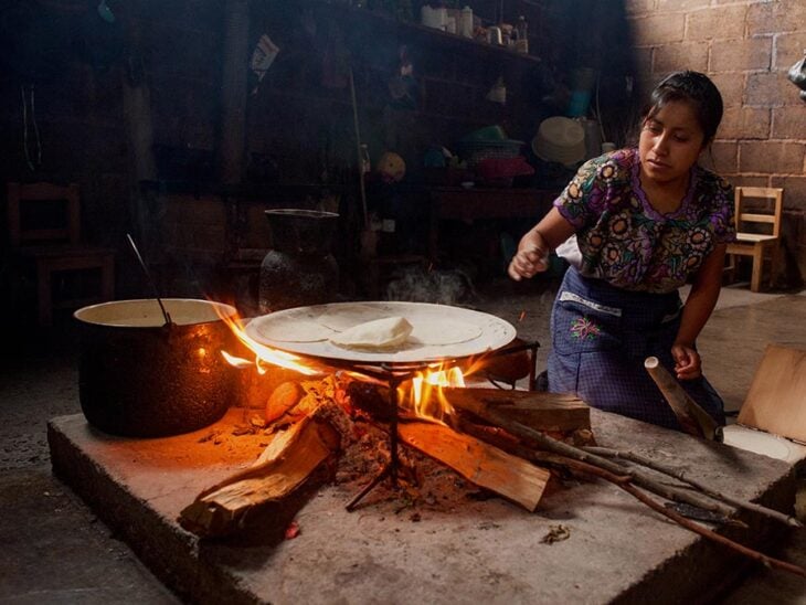 una mujer mexicana haciendo tortillas a mano en un comal en una caita de adobe