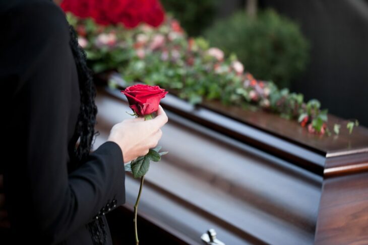 ataúd con flores y una mano con una rosa roja