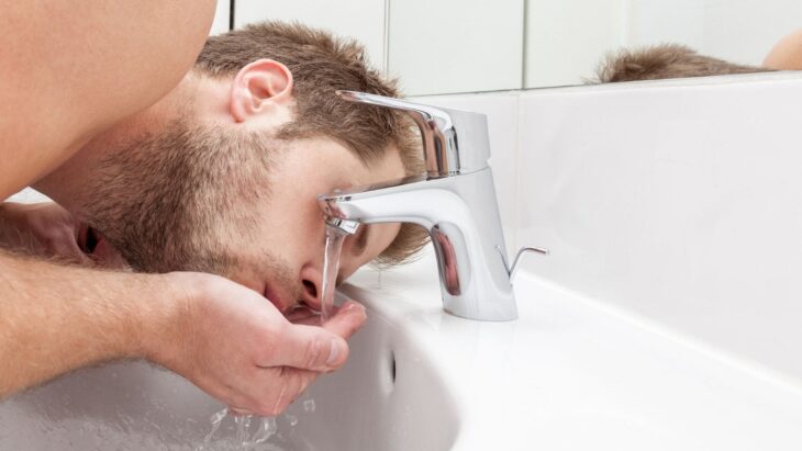 Man washing his face with tap water 