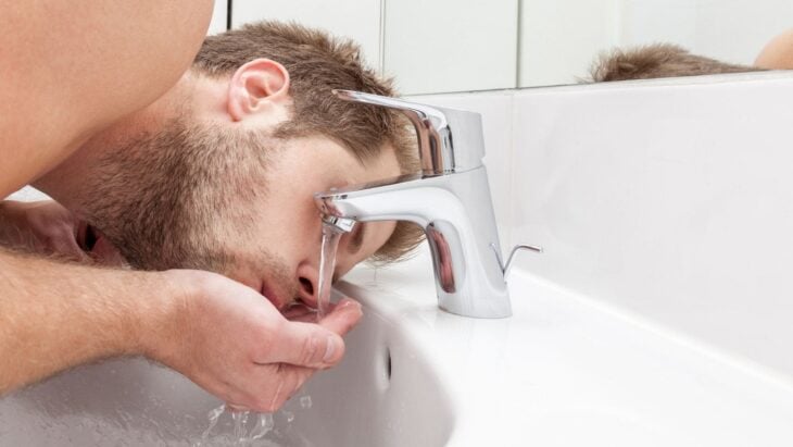 Hombre lavándose la cara con agua del grifo 