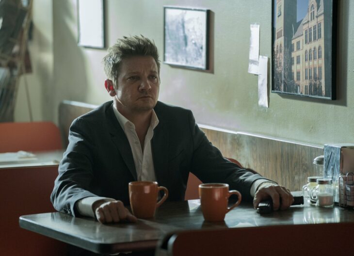 Jeremy Renner en su personaje de Mayor of Kingstown sentado en una mesa de un restaurante 