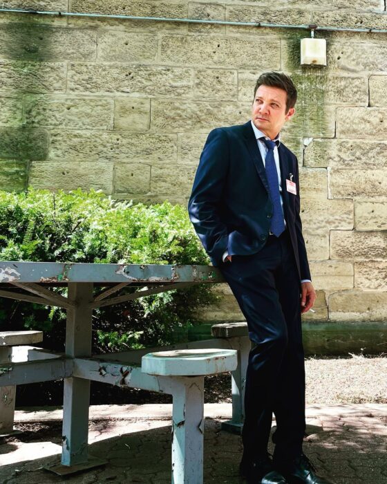 Jeremy Renner posando recargado en una mesa al aire libre 