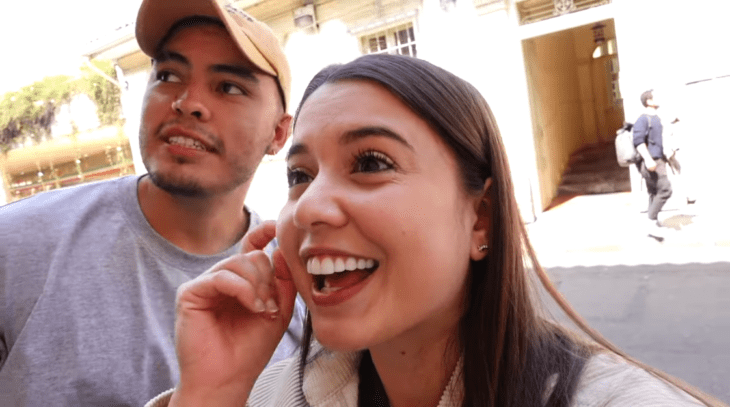 a couple look funny at a place on the street he wears a yellow cap 