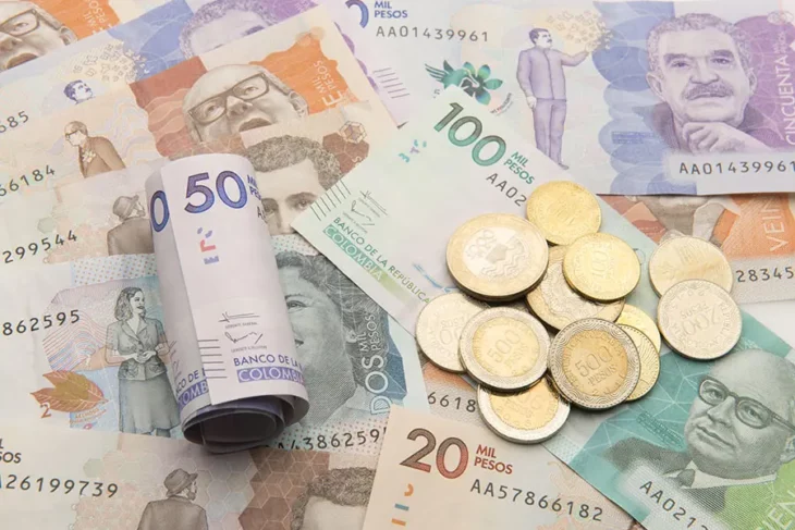 billetes colombianos de distintas denominaciones colocados en una mesa junto a oras monedas