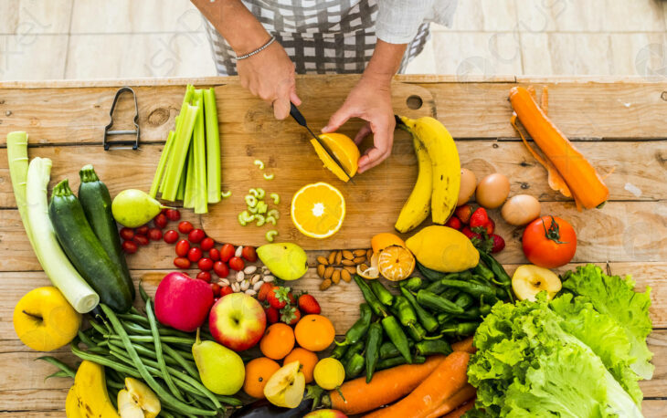 images of different fruits and vegetables placed on a table, someone is splitting an orange with a knife