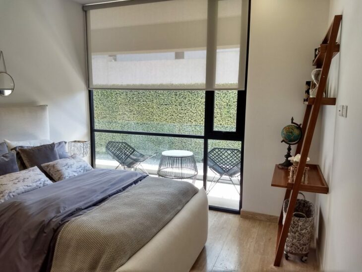 images of a bedroom in a house has a large window that overlooks an outdoor patio and a small wooden cabinet accompanies the bed