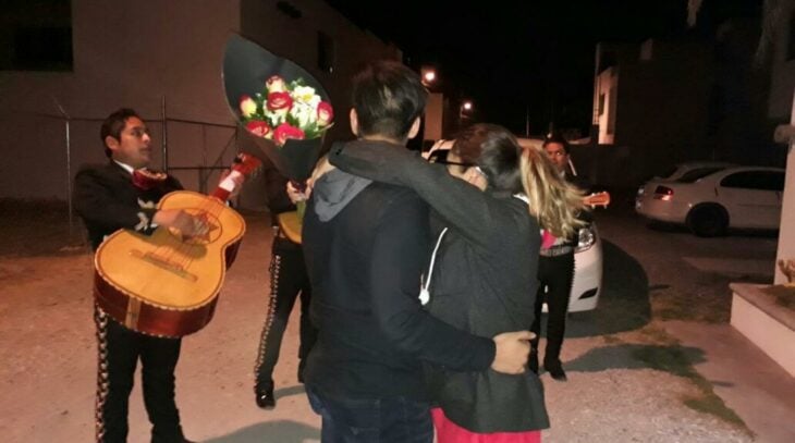 una pareja escuchando la serenata de un mariachi en la calle es de noche él novio le llevó flores