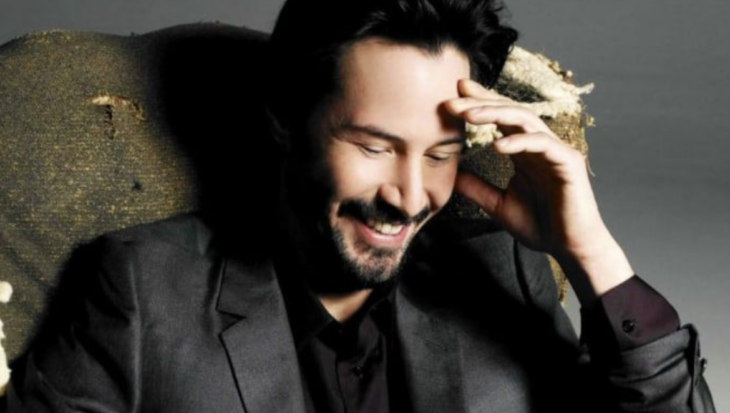 Keanu Reeves posa sonriente en una imagen donde se le observa vestido con traje gris