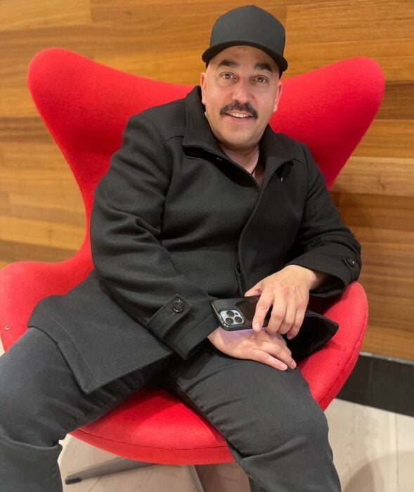 Fotografía de Lupillo Rivera sentado en un sofá color rojo 