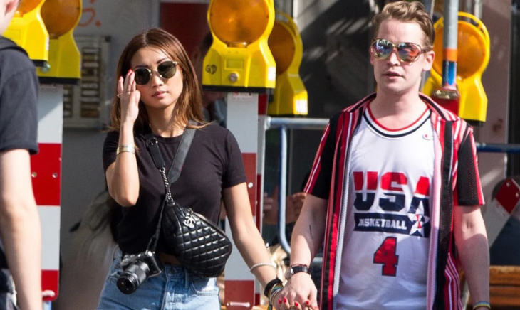 Macaulay Culkin and Brenda Song on a walk down the street holding hands and wearing sunglasses