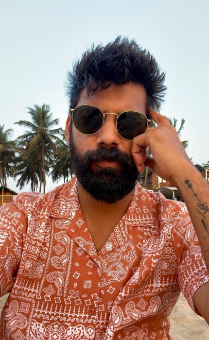 Selfie showing a young Indian man wearing an orange shirt with white figures wearing sunglasses 