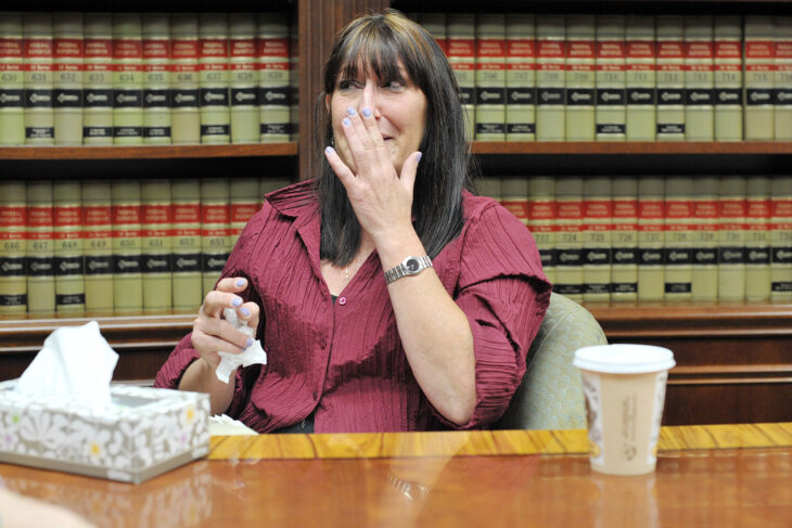 Photograph of a woman sitting at a desk crying with her hand over her face 