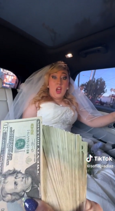 una chica vestida de novia sentada en un auto se muestra sorprendida cuando le ofrecen en un reto darle 3 mil dólares 