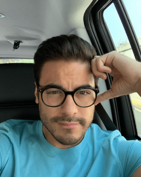 Carlos rivera with clear glasses is sitting in his car while looking at the camera