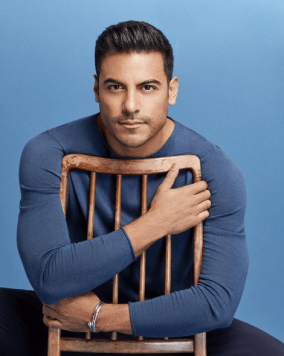 Carlos Rivera posing in a photo session is sitting on a chair hugging the back