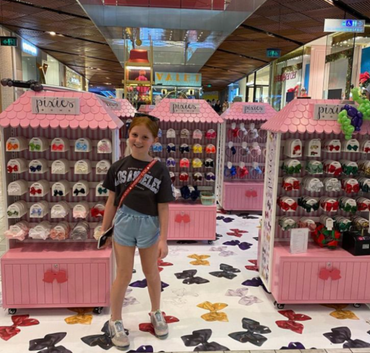 una niña parada en los estantes de una tienda departamental en el área de accesorios infantiles