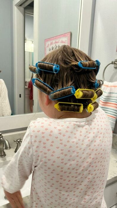 imagen de una niña de espaldas posando frente al espejo mientras se hace rizos en el cabello 