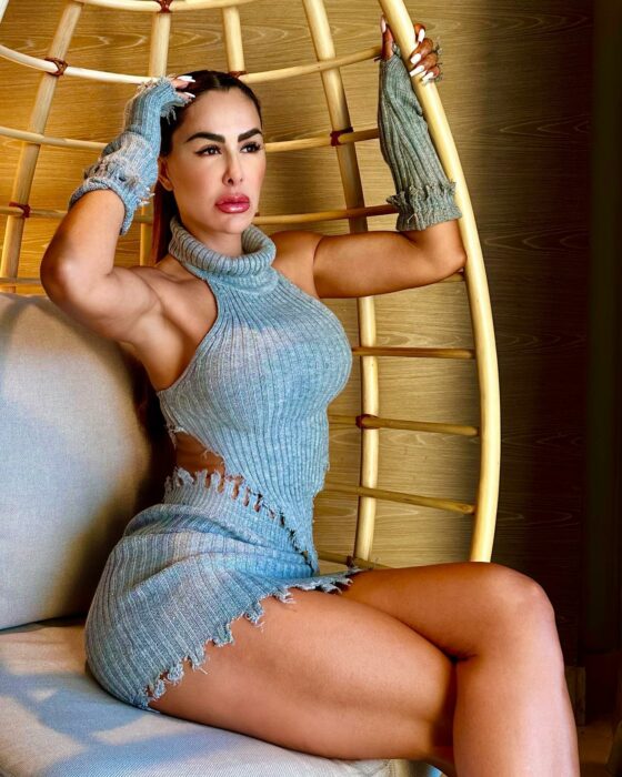 Fotografía de la cantante Ninel Conde posando sentada con un conjunto de minifalda y top en color gris 