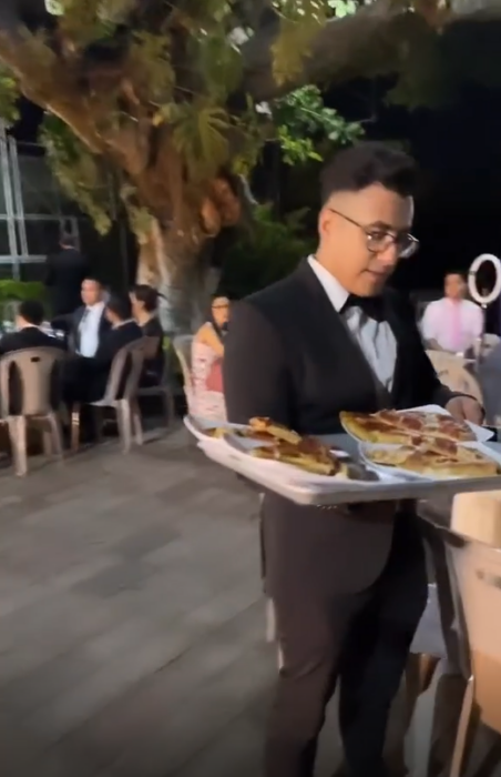 a waiter serving different dishes containing pizza with a tray is dressed in a suit