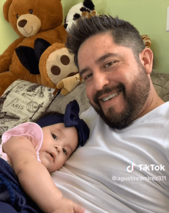 A man smiles with his little daughter leaning on his chest 