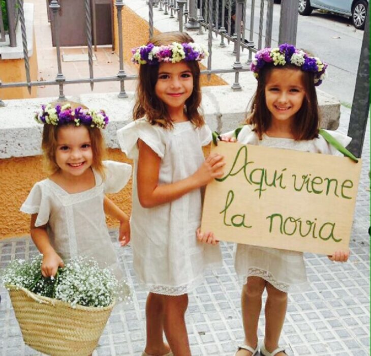 niñas vestidas para ser pajes en una boda llevan vestido blanco y corona de flores