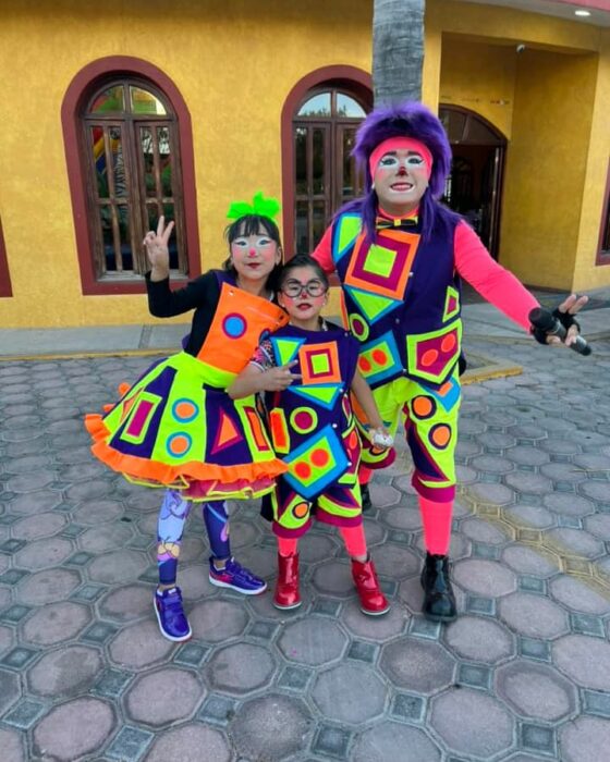 Fotografía que muestra a tres payasos posando frente a una casa 