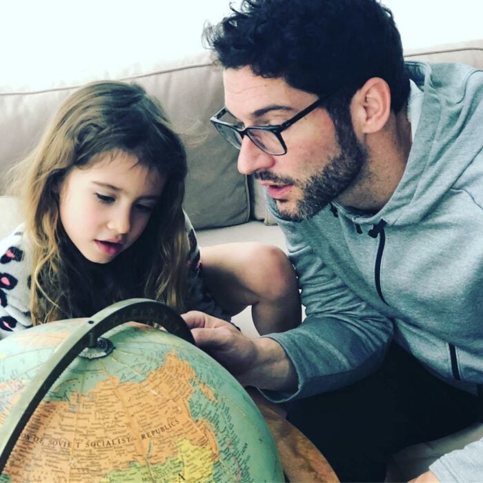 Tom Ellis junto a su hija mostrando un lugar en el globo terráqueo 