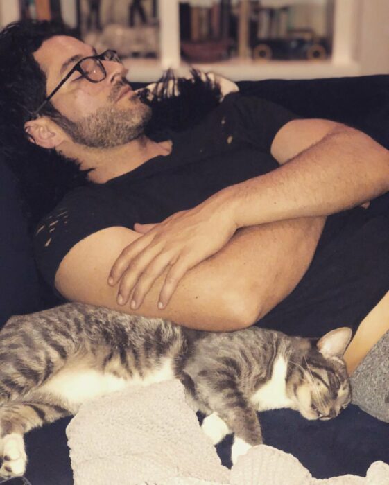 Tom Ellis acostado en un sillón rodeado de sus dos gatos 