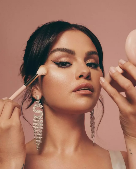 Selena Gomez posando mientras se maquilla con su nueva línea de maquillaje 