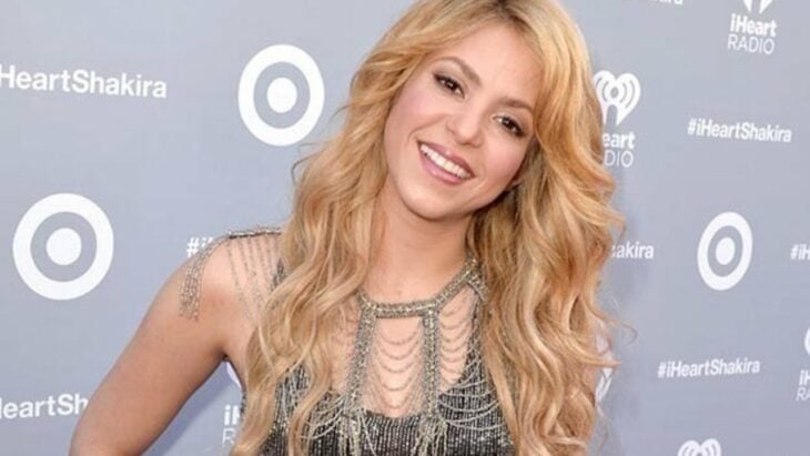 Shakira poses on the red carpet of a music event wearing a beaded dress and smiling at the camera