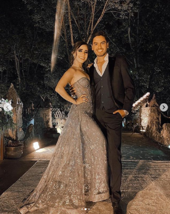 Tammy Parra y Omar Núñez posando vestidos de forma elegante afuera de un jardín